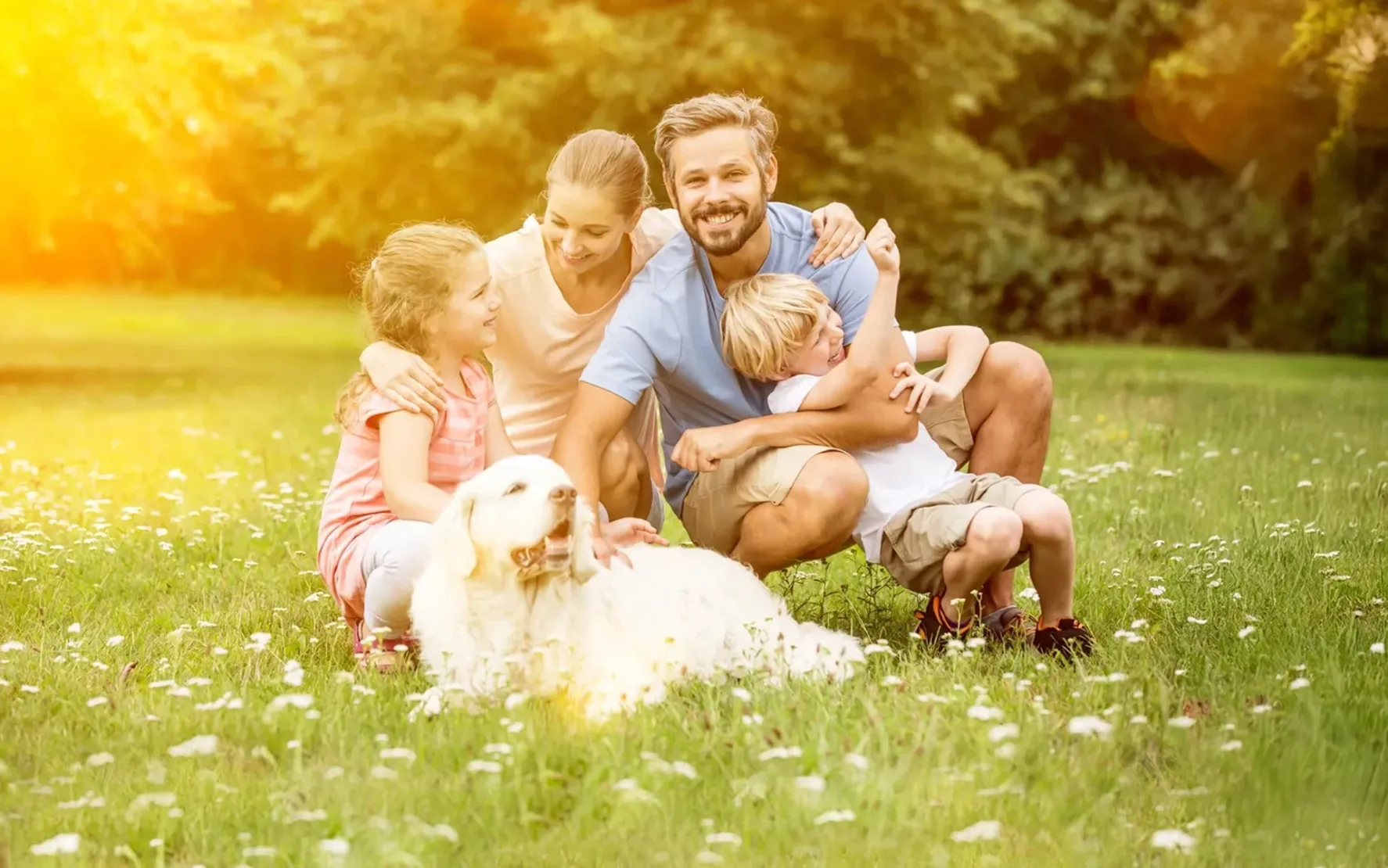 Glückliche Familie mit zwei Kindern und einem weißen Hund beim Picknick auf einer Blumenwiese im Sonnenlicht – Symbol für Lebensfreude und Naturverbundenheit.