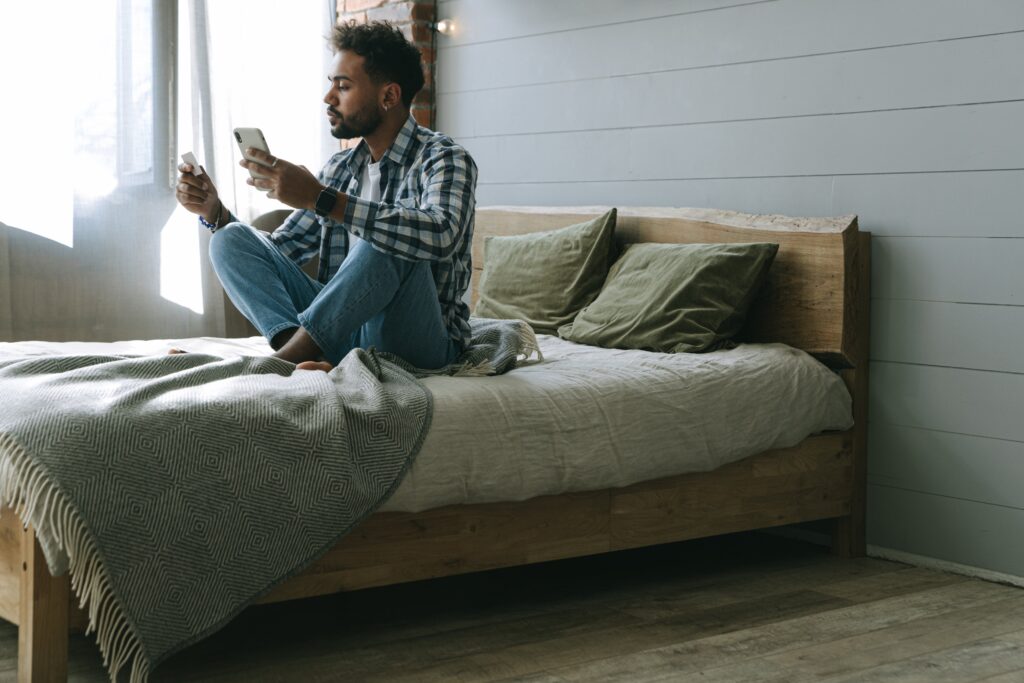 Man sitting casually on the bed with cell phone & credit card, making payments