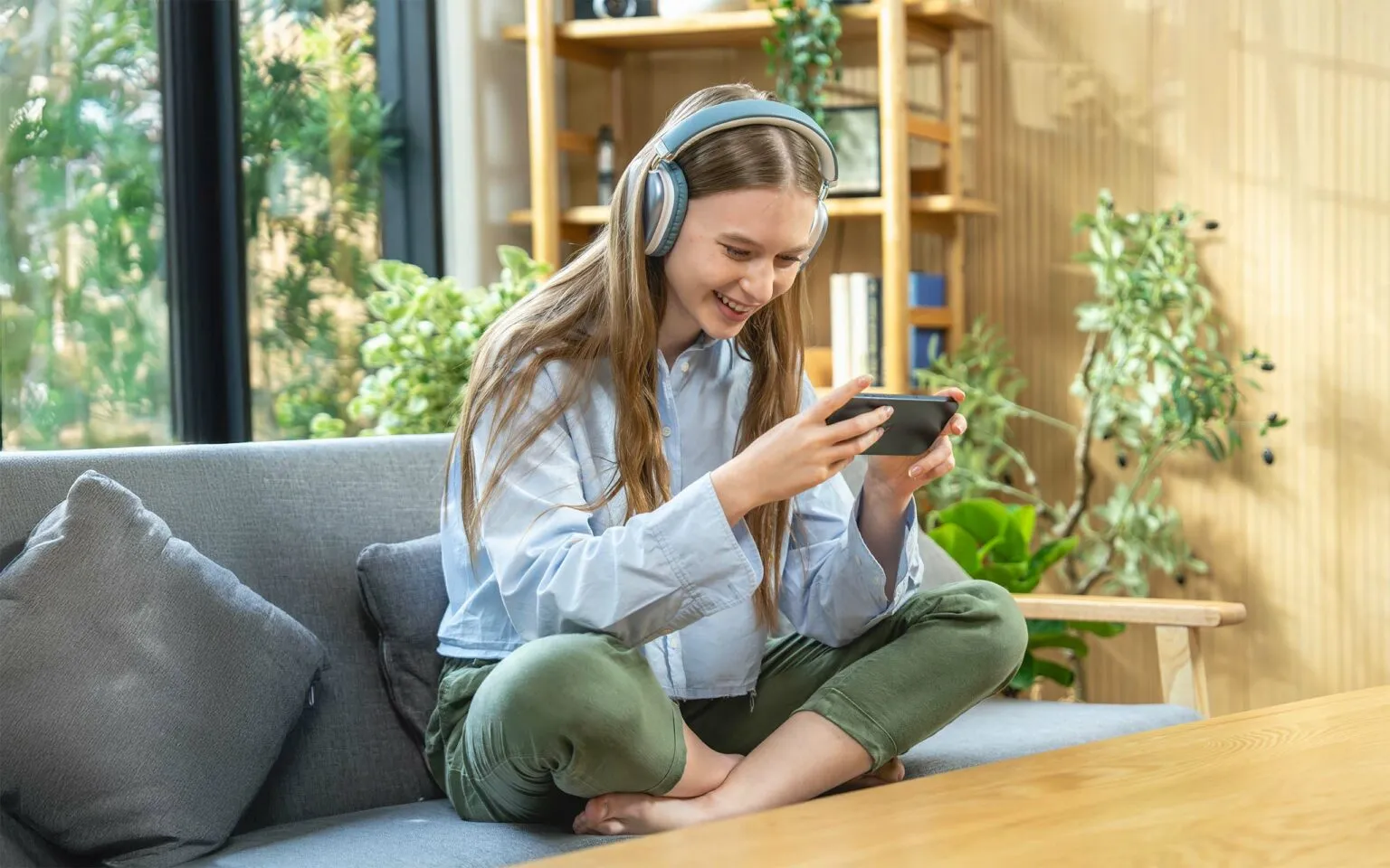 Woman Enjoying Mobile Gaming with Headphones in a Cozy Home Setting