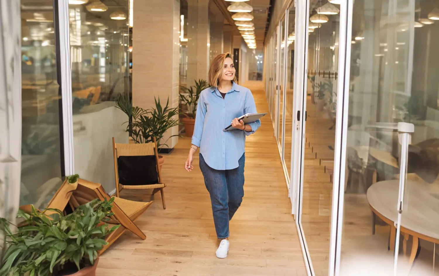 Woman in blue dress shirt and blue denim jeans standing beside brown wooden chair