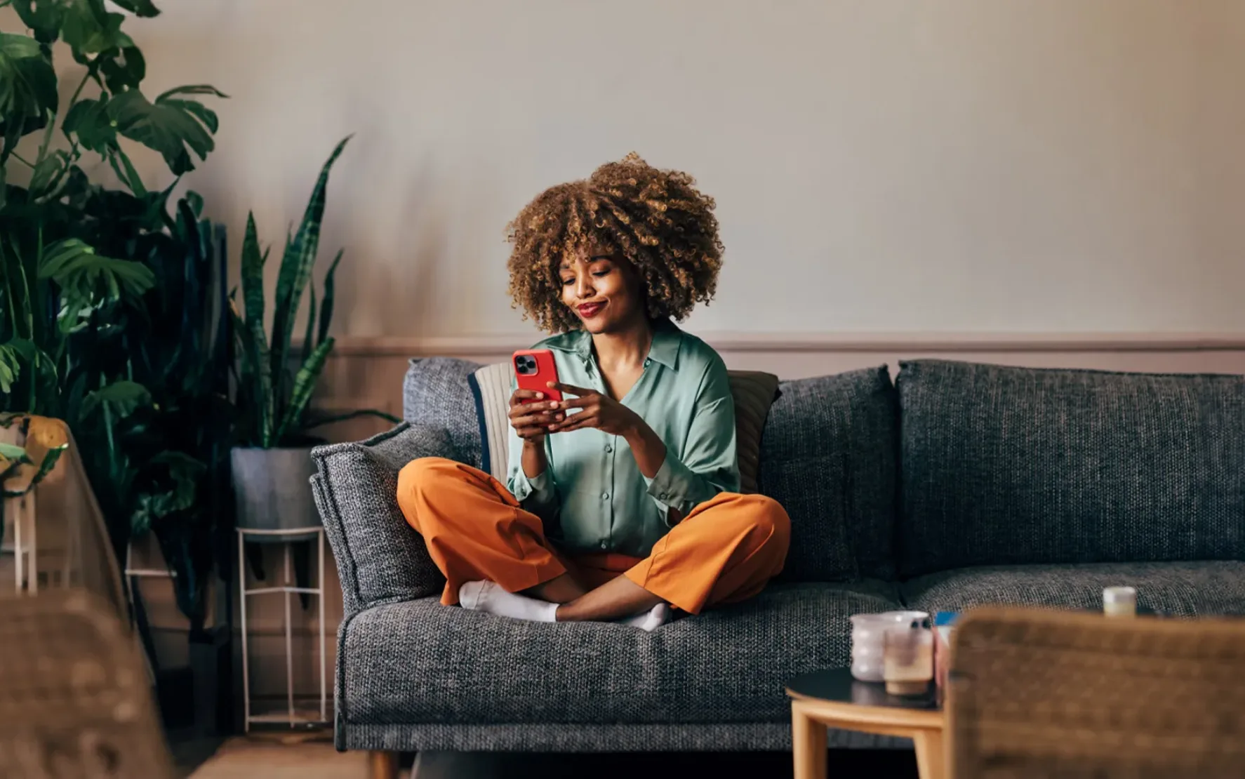 A smiling elegant female using her smartphone while sitting on the cozy sofa in the living room.